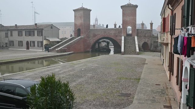 Comacchio, Italy. December 2019. Tilt shot on the characteristic bridge called Trepponti. On the right the facade of a house with colored cloths that are hung out to dry.