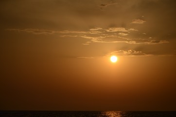 Beautiful sunset sky and a small ball of sun setting over the horizon above the sea surface