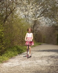 Young girl riding scooter on path through park