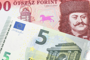 A close up image of a red, one hundred Hungarian forint bill close up with a blue and green five euro note from Germany in macro