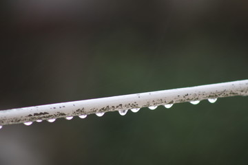 Reflecting raindrops hanging from outdoor rusting metal rod.