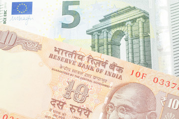 An orange, Indian ten rupee bill, close up with a blue and green five euro note from France