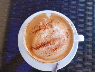 a Cup of cappuccino with cinnamon on a wicker table, top view