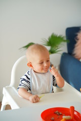 Mom feeding her baby girl with a spoon. Mother giving food to her eight-month child at home.