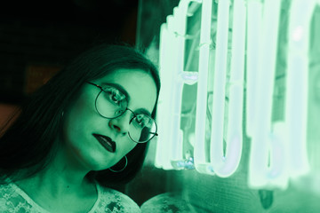 young woman with glasses with reflections of a neon signboard