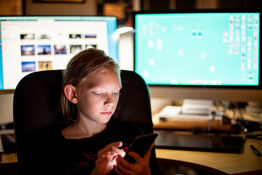 Boy using smart phone in front of computers