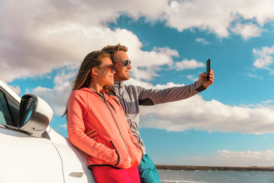 Selfie couple tourists on road trip travel taking photo with phone at summer vacation car rental. Young woman and man friends smiling in sunglasses outdoor in Europe.