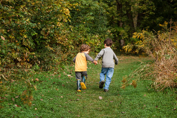 Behind view of two small boys holding hands and running through park