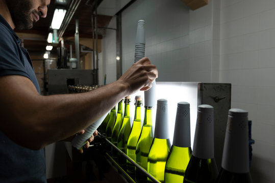Man placing white foil wrap on bottles on conveyor