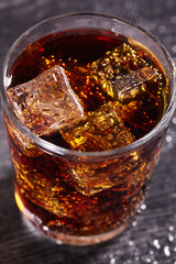 Transparent glass of cola with ice cubes on wood table. Close up.