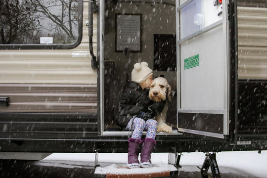 little girl sitting outside on steps of camper with big dog in snow