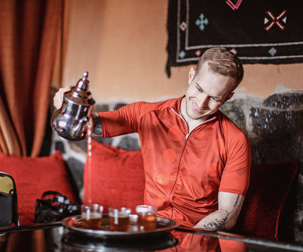 A young man pours a traditional cup of Moroccan Tea from a kettle
