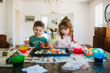 Young boy and girl sitting at kitchen counter dying easter eggs