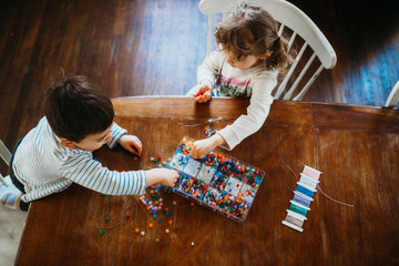 Young brother and sister picking beads to making bracelets at home