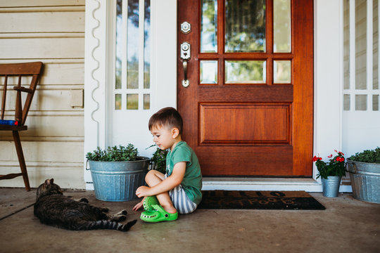 Young boy sitting outside front door petting short hair cat