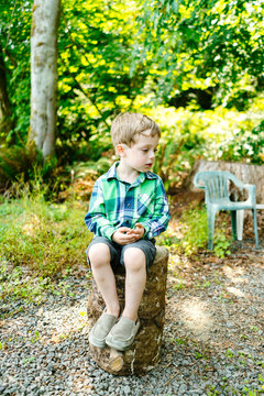 Straight on view of a young boy sitting on a log stool