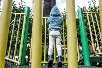 view of little girl from behind standing on tip toes on playground