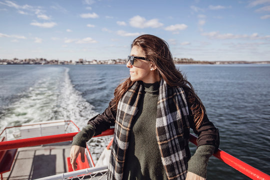 A woman leans against the railing of a ferry on a sunny day in Maine