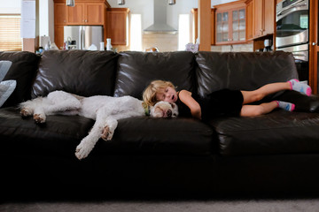 little girl laying on couch yawning with dog