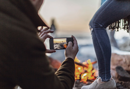 A man takes a picture of a campfire with a cell phone