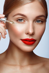 Beautiful girl with red lips and classic makeup with oil for skin in hand. Beauty face.