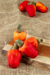 Red cashew fruit with raw cashews nut. In a piece of wood,.  With old bag background. Fresh e colorful fruits.