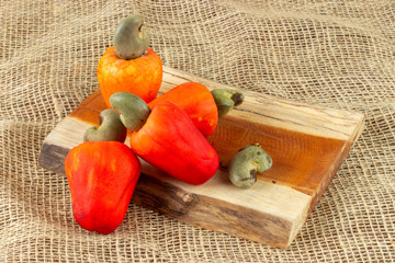 Red cashew fruit with raw cashews nut. In a piece of wood,.  With old bag background. Fresh e colorful fruits.