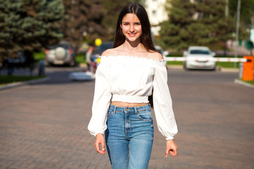 Young beautiful brunette woman in jeans and white blouse walking in summer street