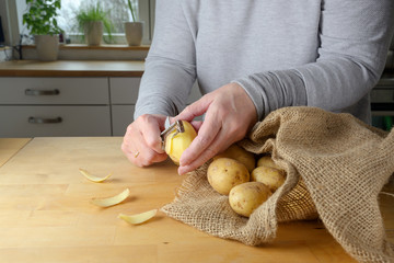 Hands of a woman are peeling raw potatoes on a wooden table in the kitchen at home
