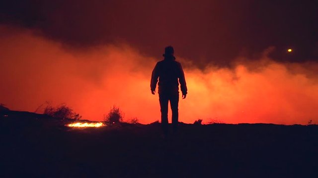 Silhouette of a man walking to the edge of a cliff, revealing burning nature, at the Australian bushfires, at night time, in New South Wales, Australia