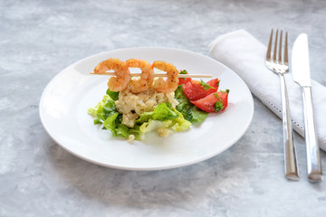 festive appetizer from shrimp skewers on a cauliflower risotto heap, lettuce and  tomatoes on a white plate, light gray background with copy space