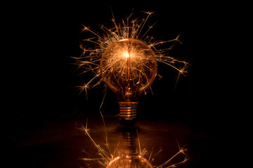Electric tungsten lightbulb on a black background emitting sparks