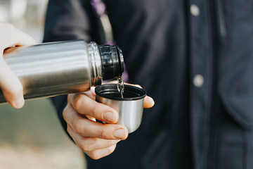 Person holding a thermos and pouring hot tea into the cup in the forest. Hot drinks concept. 