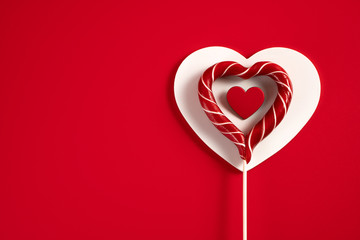 Heart-shaped Lollipop with red hearts on a white wooden heart on a red background for Valentine's Day, wedding and other holidays, view from the top.