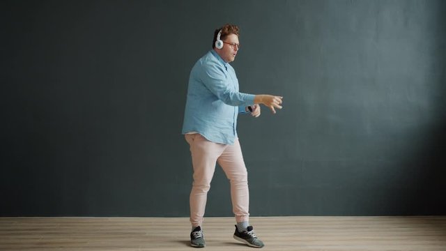 Carefree guy is dancing robot dance on black background having fun alone indoors enjoying song in wireless headphones. People and modern devices concept.