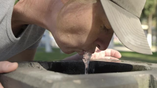 Woman drinks spring water from city fountain closeup.