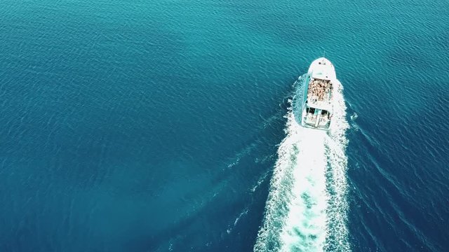 fast white yacht sailing the turquoise sea, leaving traces of white sea foam, people on the yacht dancing, party on the yacht, top view, slow motion