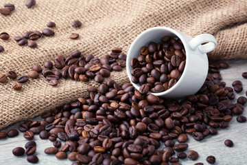 Coffee beans on light wooden background. Roasted coffee beans, white cup, sackcloth, can be used as a background