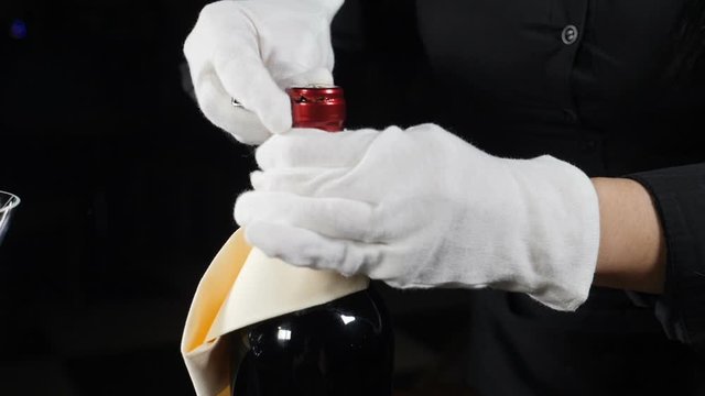 Close-up shot of wine bottle being uncorked. Waiter in white gloves shot on black background. foil being cut off. Slow motion. Full hd