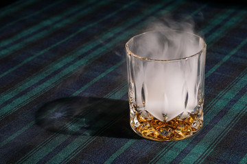 A glass of whisky with smoke on tartan