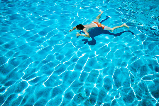 Unrecognizable young man doing an underwater crawl in a bright blue swimming pool