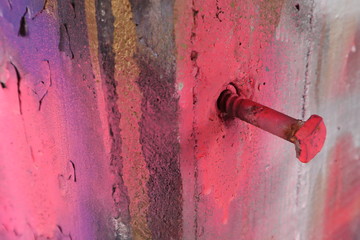 Closeup of a large painted screw sticking out of an old cement wall
