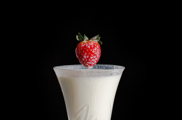 Strawberries falls in a milk in the dark room