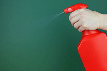 A Hand Using A Hand Held Sprayer To Spray Water Against A Dark Green Background.