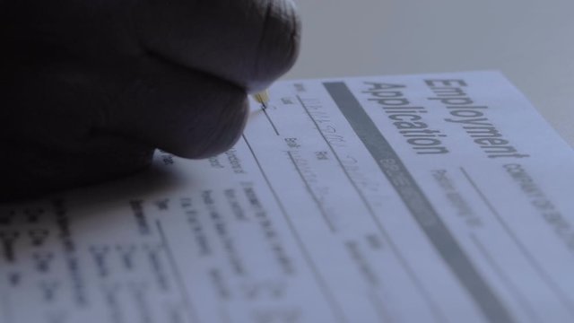 black man's hand filling out employment application form