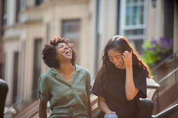 Fototapeta premium Female friends laughing while standing against houses in city