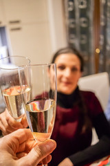 People having fun together toasting drinks in the home kitchen. Happy and smiling woman toasts with flute of sparkling wine (champagne). Focus on central glass. Friendship, love and family concept.
