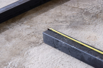 Measuring tape on black square huge pipe on concrete floor.