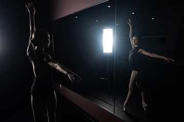 Fototapeta na wymiar Young dancer in dark room looking at mirror