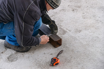 A builder draws on a square metal pipe using a locksmith on the concrete floor.